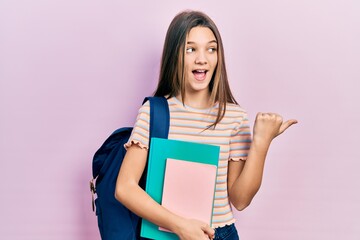 Sticker - Young brunette girl holding student backpack and books pointing thumb up to the side smiling happy with open mouth