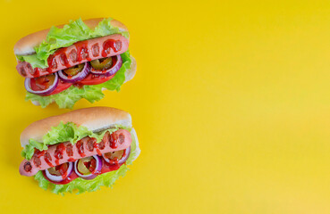 Wall Mural - Homemade hot dog made of grilled sausage with tomato slices, onion rings and lettuce leaves garnished with ketchup served in sliced bun laying on bright yellow background. Image with copy space