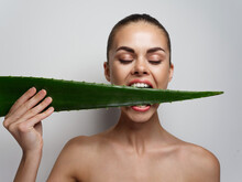 Woman With Snow-white Teeth Bites Green Aloe Leaf On Light Background 