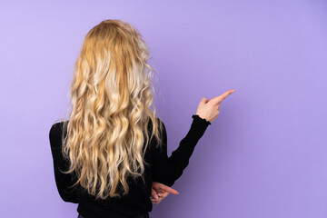 Canvas Print - Young blonde woman isolated on purple background pointing back with the index finger