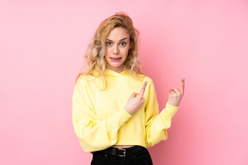 Canvas Print - Young blonde woman wearing a sweatshirt isolated on pink background frightened and pointing to the side