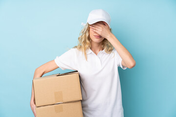 Poster - Young delivery woman isolated on blue background covering eyes by hands