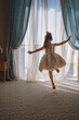 © Yulia Raneva - Back view of little girl in white dance dress dancing by the window in luxury apartment bedroom and looking out at the sea. Image with selective focus