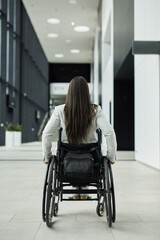 Wall Mural - Vertical back view portrait of young businesswoman in wheelchair entering office building