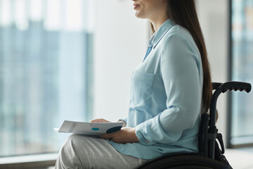 Wall Mural - Cropped side view portrait of young businesswoman in wheelchair holding booklet while giving speech or attending conference, copy space