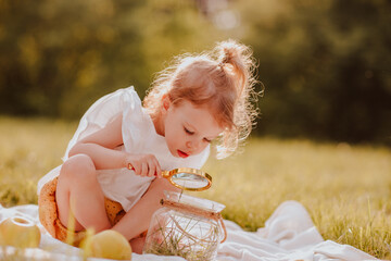 Girl playing with magnifying glass in the park. Summertime. Copy space.