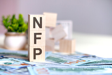 wooden cubes with the letters NFP arranged in a vertical pyramid on banknotes, concept