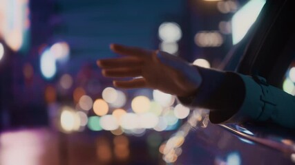 Wall Mural - Female is Commuting Home in a Backseat of a Taxi at Night. Passenger Chilling and Holding Her Hand Outside of Window while in a Car in Urban City Street with Working Neon Signs. Cinematic Footage.