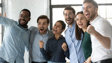Multiethnic Team Of Excited Employees Celebrating Corporate Achievement, High Sales Result, Work Success, Shouting For Joy. Happy Diverse Professionals Hugging, Laughing, Making Winner Gestures