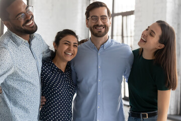 Wall Mural - Happy diverse business team celebrating corporate success together. Excited office colleagues hugging in contemporary workspace, smiling, laughing, having fun. Teamwork, reward, achievement concept.