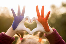 Love And Happiness Concept. Cute Child Forming Heart Gesture With Hands Outdoors On Nature Sunset Bokeh Background. Heart Shape Of Kids Hand Painted In France Flag Colors, Kids Body Language