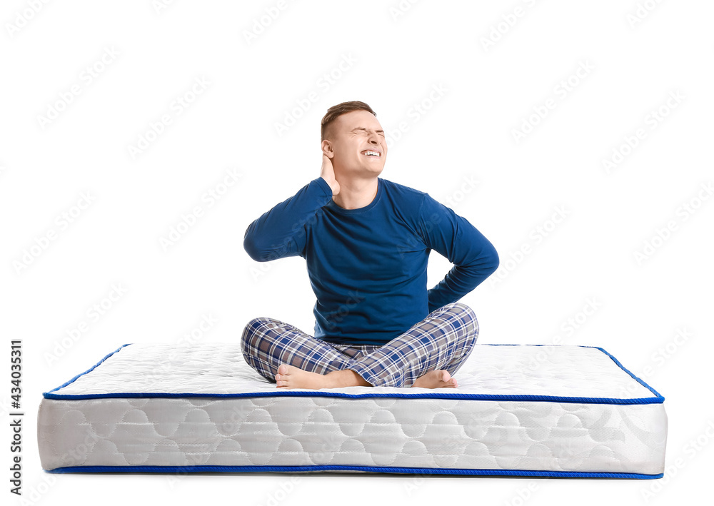 Young man suffering from pain on mattress against white background