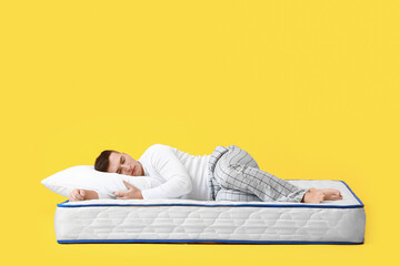 Young man sleeping on soft mattress against color background