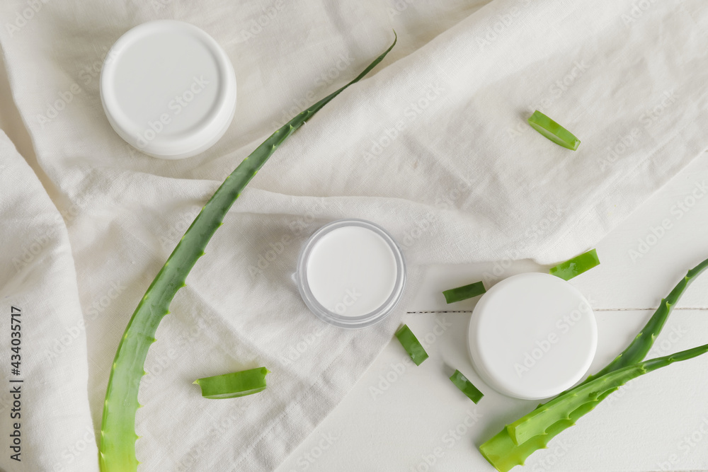 Jars with cream and aloe pieces on light wooden background