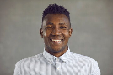 Studio portrait of happy young black man with stubble on shaved face smiling at camera with sincere positive emotions. Headshot of friendly businessman, salesperson, manager, or white collar worker