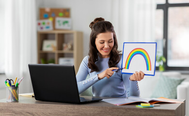 Wall Mural - distant education, school and people concept - happy smiling female teacher with laptop computer and picture of rainbow having online art class at home