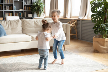 overjoyed two small preschooler girls children have fun dancing together in cozy living room holding