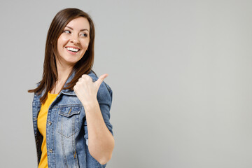 Wall Mural - Young smiling caucasian woman 20s wear casual trendy denim jacket yellow t-shirt point thumb finger back aside on workspace copy space area mock up isolated on grey color background studio portrait