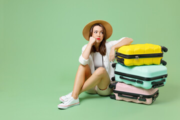 Full length thoughtful traveler tourist woman in casual clothes hat sitting near many suitcases valises isolated on green background Passenger travel abroad weekend getaway Air flight journey concept