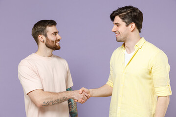 Two caucasian happy young men friends together in casual t-shirt tattoo translate fun hold hands folded handshake gesture, greet isolated on purple background. People lifestyle friendship concept