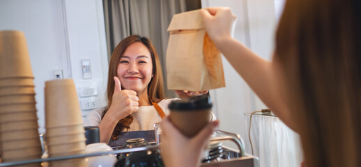 Wall Mural - A waitress making and showing thumbs up hand sign while serving a takeaway food in paper bag to customer in a shop