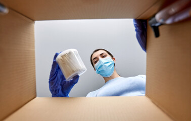 Wall Mural - home delivery, shipping and pandemic concept - woman in protective medical mask and gloves unpacking parcel box with cosmetics and beauty products