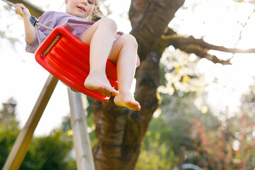 closeup of feet of little toddler girl having fun on swing in domestic garden. small child swinging 