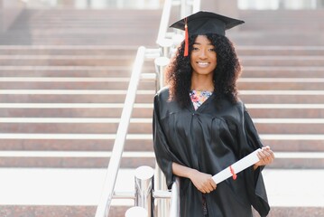 Wall Mural - cheerful afro american female graduate standing in front of university building