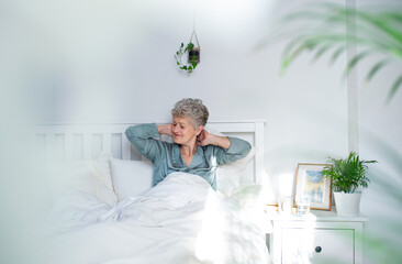 Wall Mural - Senior woman in bed at home getting up in the morning, stretching.