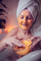 Wall Mural - Happy senior woman applying beauty face mask in bath tub at home, relaxing.