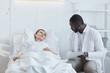 © Seventyfour - African doctor with medical card talking to patient who lying on hospital bed