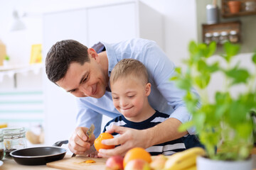 Father with happy down syndrome son indoors in kitchen, preparing food.