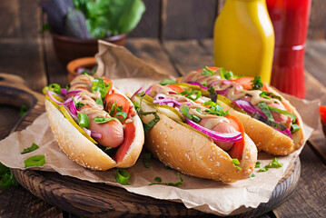 Wall Mural - Hot dog with  pickles, tomato and lettuce on wooden background. Hotdog, american cuisine.