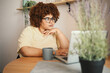 © Алина Троева - Attractive happy stylish plus size African black woman student afro hair in glasses studying online working on laptop computer at home office workspace. Diversity. Remote work, distance education