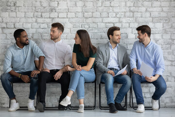 Wall Mural - Vacancy applicants talking, discussing employment and hiring, waiting appointment with employer in corridor. Queue of candidates expecting job interview, holding resume, sitting on chairs, chatting