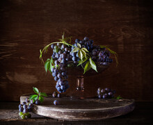 Still Life In Classic Old Dutch Style With Blue Grapes On A Wooden Stand, Dark Background. High Quality Photo