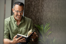 Mature Man Reading Book By Window, Smiling Wearing Glasses, Copy Space