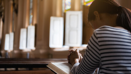 Wall Mural - Christian woman praying on holy bible in the public church. Woman pray for god blessing to wishing have a better life and believe in goodness.