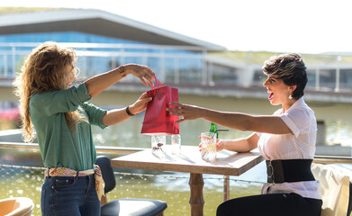 Two female friends giving each other gifts while being surprised happily