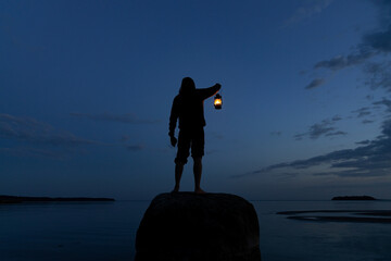 man standing on the rock and holding old lantern outdoors near the sea at night. light and hope conc