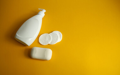 white dispenser bottle with a bar of soap with cotton pads and ear sticks on a yellow background