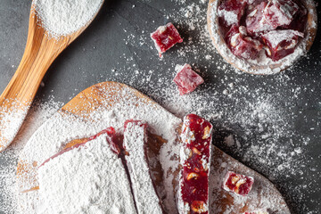 making of delicious fruit flavored homemade Turkish delight with vibrant pink red color and mixed with hazelnuts. Sifted Confectioners sugar is added on top and  dice shaped pieces were cut out.