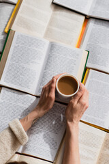 Wall Mural - cropped view of woman holding cup of coffee near open books