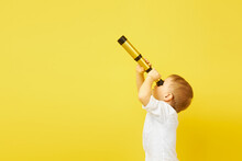 Side View Of A Child Looking Through A Telescope On A Yellow Background. The Concept Of Travel, Pirates And Adventures, Active Lifestyle, Striving For The Goal