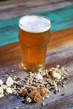 Glass Jug Of Beer With Froth Against Spilled Barley Grains And Bread Pieces On Painted Table