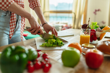 Close-up of the hand only view of a woman slicing a salad, preparing for a healthy organic vegetarian meal with chilli peppers and broccoli. On the background of the kitchen