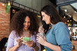 © Julio Rodriguez/ADDICTIVE STOCK - Smiling young female friends wearing casual clothes browsing mobile phones while having a soda in restaurant