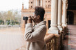 © Julio Rodriguez/ADDICTIVE STOCK - Side view young African American female photographer in warm coat taking pictures of historic city buildings on modern photo camera on early spring day