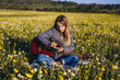 © Macia Puiggros/ADDICTIVE STOCK - Young hipster woman sitting on a meadow in the countryside writing songs on notebook and playing guitar during summer sunlight.