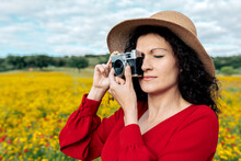 Smiling Female In Hat Taking Photo On Vintage Camera On Meadow Under Cloudy Sky